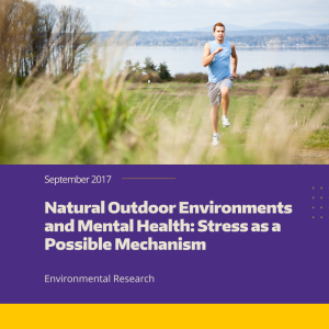 A person runs through a park with a body of water and mountains in the background