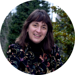 A photo of Kathy smiling in front of evergreen trees