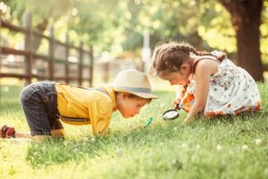 Two children looking in the grass with magnifying glasses.