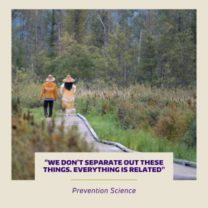 Two Indigenous Canadian women walking on a boardwalk trail in a wetland. They are wearing traditional clothing.