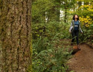 A young adult walking through the forest and looking at trees while wearing headphones