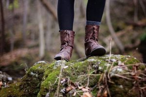 A person wearing hiking boots stands on a moss-covered rock