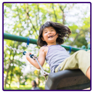 A young Asian child swinging with a forest in the background