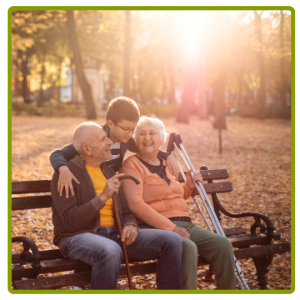 Two grandparents sitting on a park bench. Their grandchild hugs them from behind.