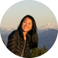 A photo of Janelle smiling with mountains and evergreens in the background