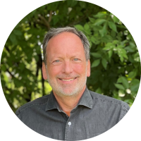 A headshot of Marc Berejka smiling in front of trees