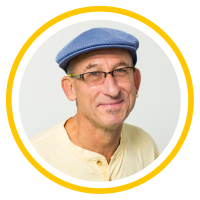 Daniel wears a blue hat, glasses, and a yellow shirt. He has a slight smile.
