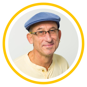 Daniel wears a blue hat, glasses, and a yellow shirt. He has a slight smile.