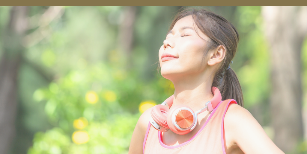 A person stands in the forest with their eyes closed, breathing deeply
