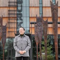 Owen Oliver stands in front of the Guests of the Great River display at the Burke Museum. The piece consists of 11 large-scale bronze paddles representing the arrival of a Chinookan canoe carrying cultural heroes of the Columbia River region, and with them the knowledge they embody. 
