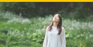 A person breathing deeply with their eyes closed in a forest